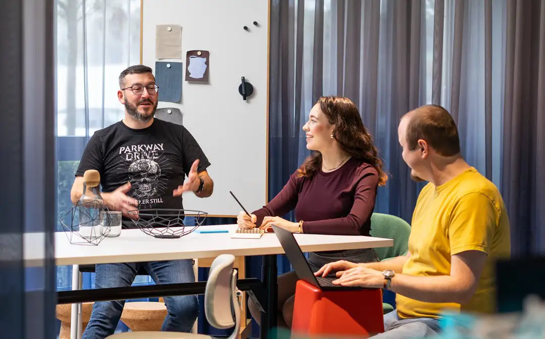 Diskussionen am Tiscch Drei Teammitglieder sitzen an einem Tisch in einem Büro und tauschen sich über individuelle Softwareentwicklung aus.