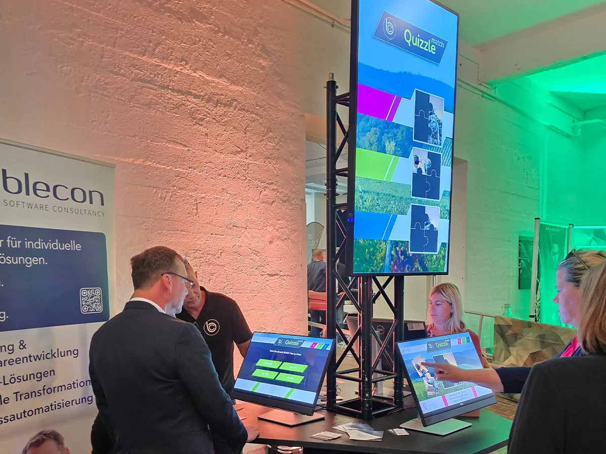 Interaktives Quiz-Erlebnismodul von blecon im Messebetrieb mit Touchscreens und zentralem Großbildschirm zur Besucheraktivierung.