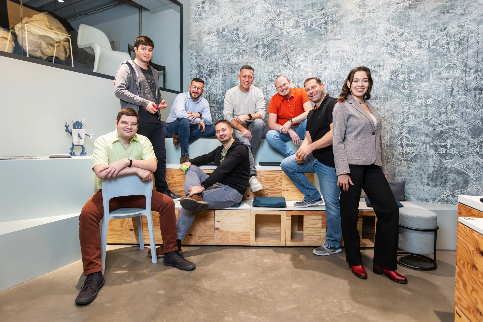 Gruppenfoto des blecon-Teams in einem modernen Büro; mehrere Teammitglieder sitzen und stehen entspannt zusammen und lächeln in die Kamera.